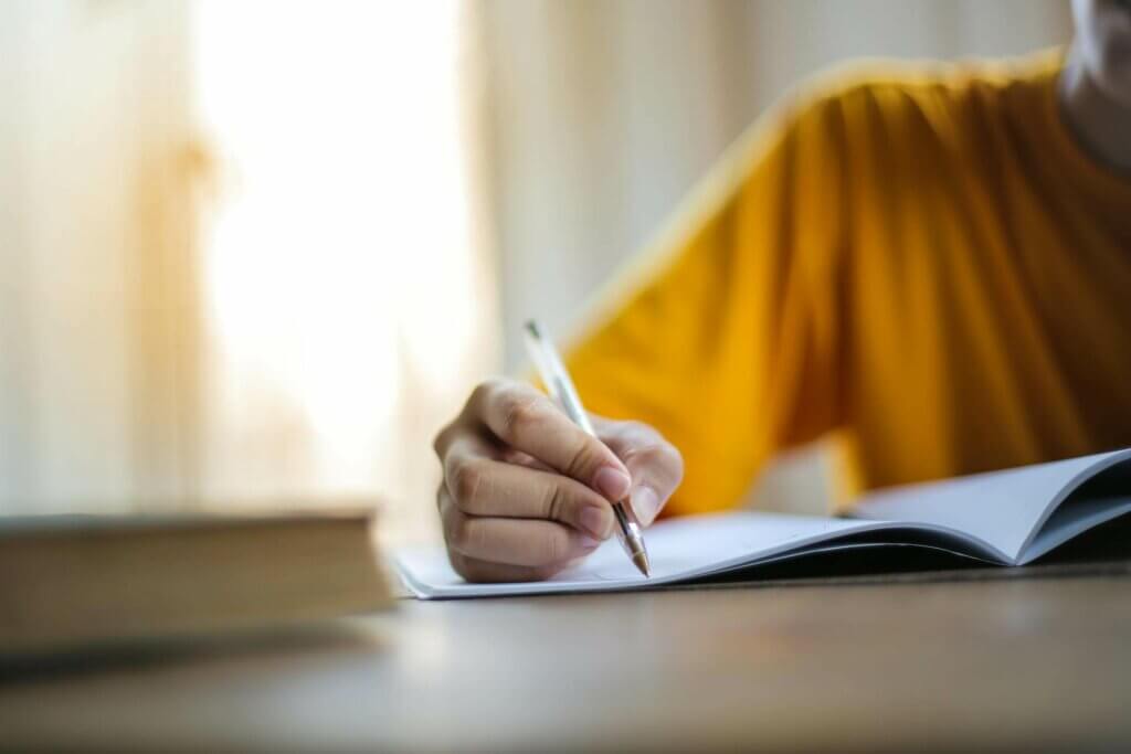 Main d'adolescent en train d'écrire sur un cahier pour illustrer l'accompagnement en orthopédagogie de L'Embellie Sophro, sophrologue et orthopédagogue à Mouchin, Pévèle