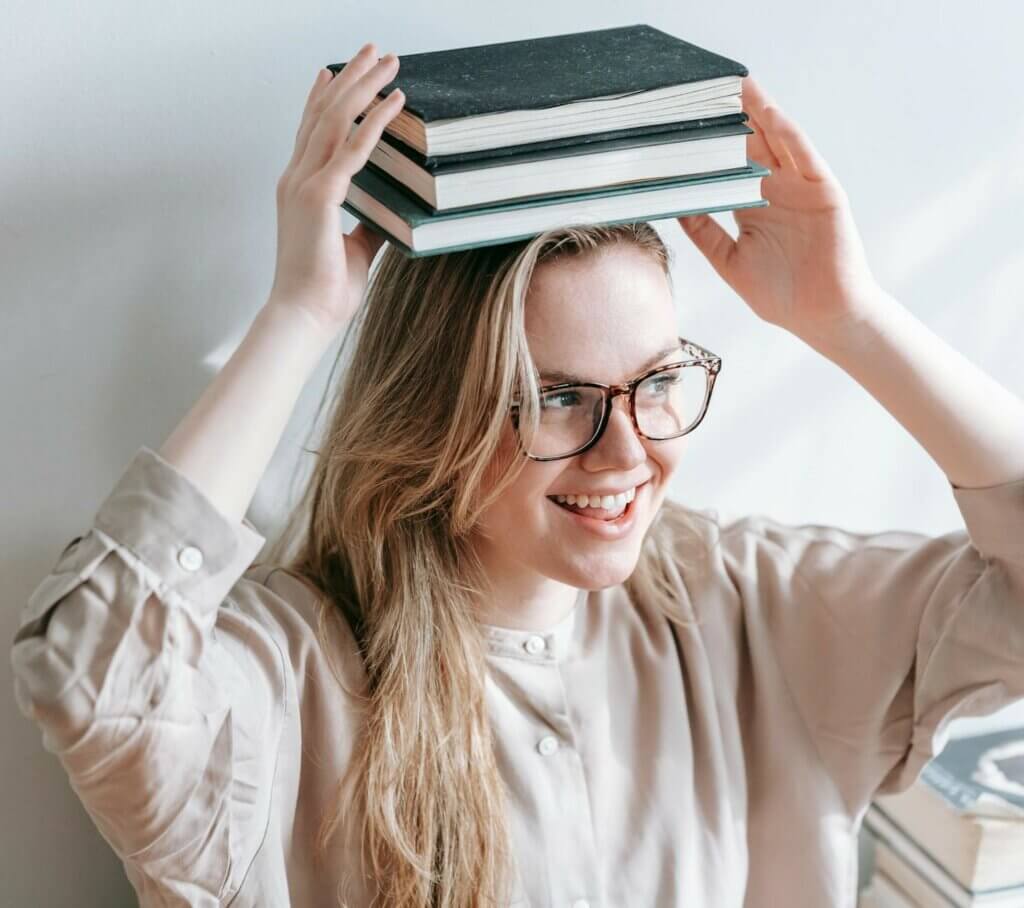 Adolescente qui pose des livres sur sa tête en souriant - L'Embellie Sophro, sophrologue et orthopédagogue à Mouchin, Pévèle